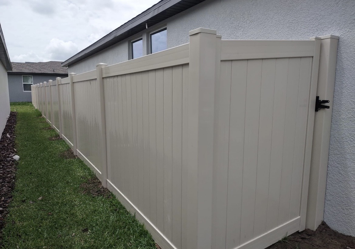 Tan vinyl privacy fence with gate along a house
